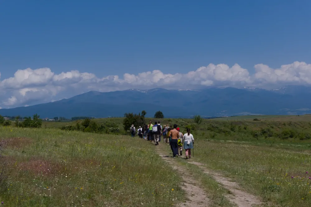 a line of Green Pathways participants hiking across a highland meadow near Bansko, the Pirin mountains behind
