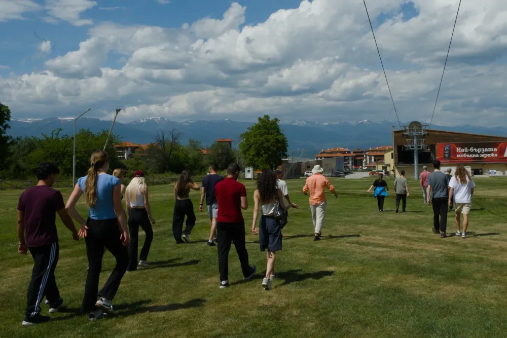 participants walking across a field in Bansko, snow-capped mountains and the town's cable car station behind