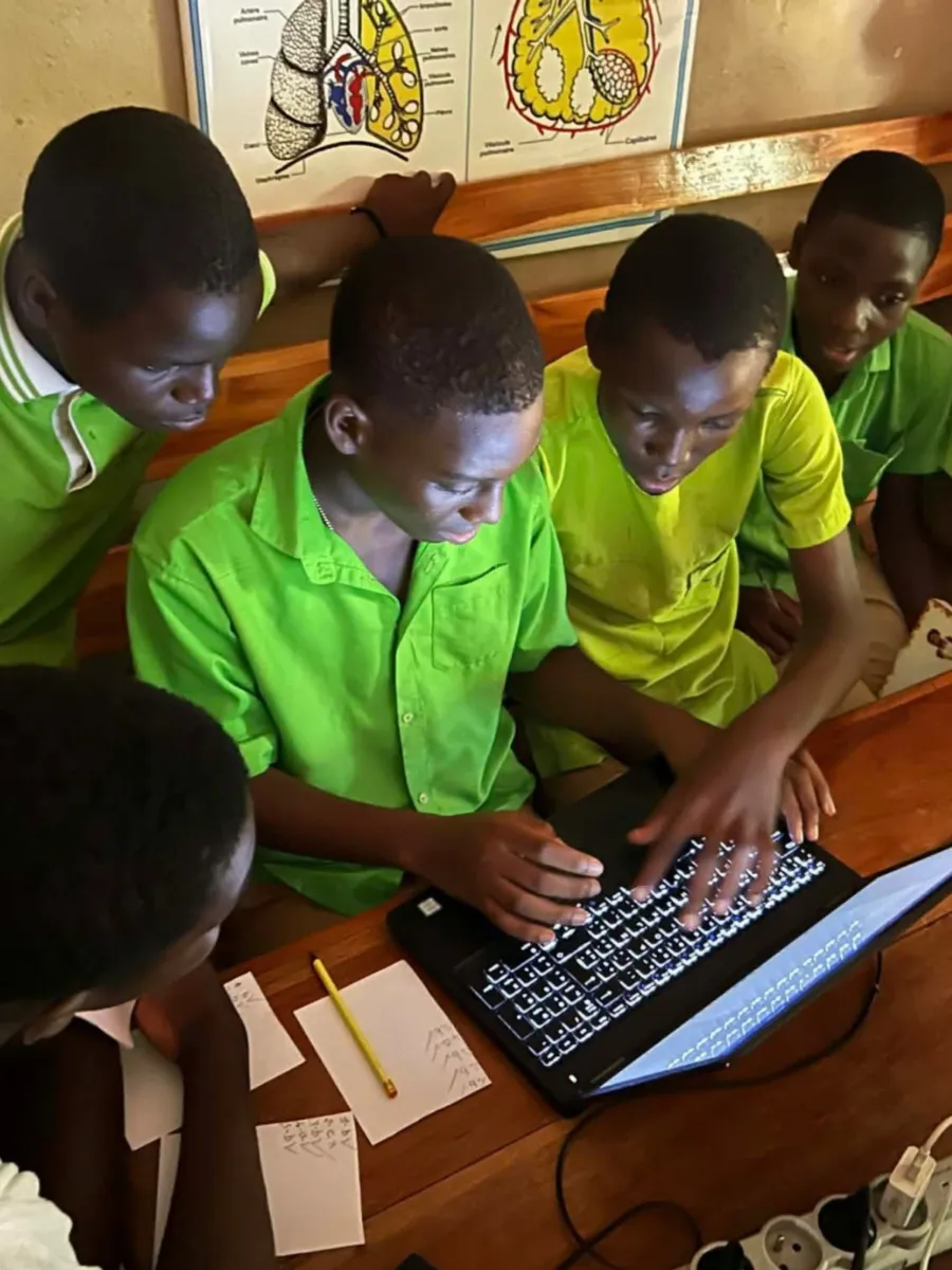 five students crowding around a single shared laptop at La Voie School